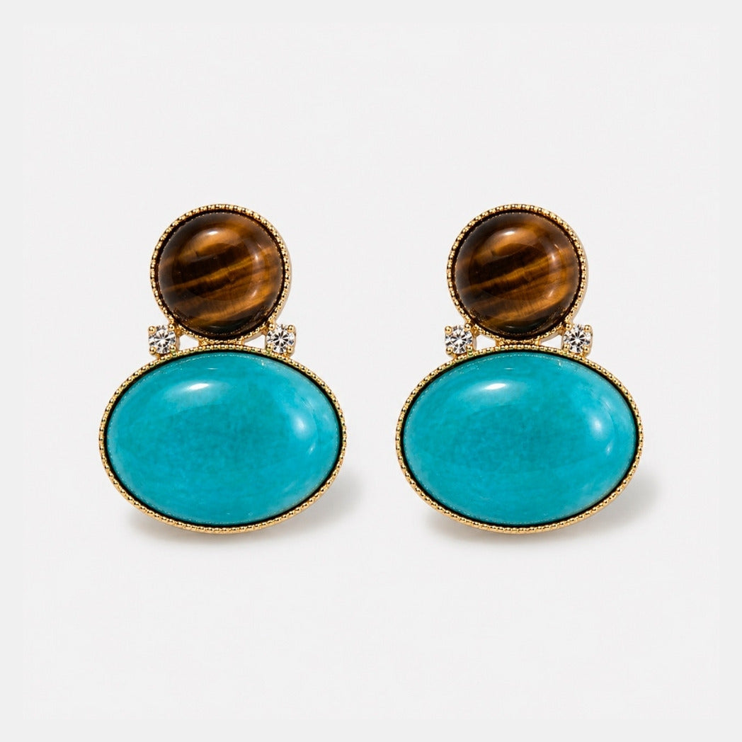 A pair of gold-tone drop earrings featuring a round brown tiger's eye stone on top and a larger oval turquoise cabochon below, accented with small clear crystals, set against a light gray background.