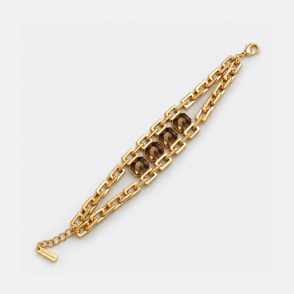 A gold-tone chain bracelet with three central oval links featuring dark brown faceted stones, displayed diagonally on a light gray background.