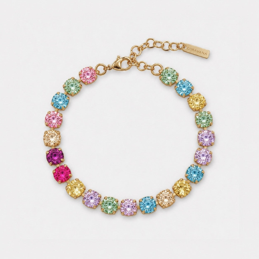 A gold-tone bracelet featuring multiple round, colorful gemstones in pink, blue, green, yellow, and purple, arranged in a rainbow pattern on a light gray background.