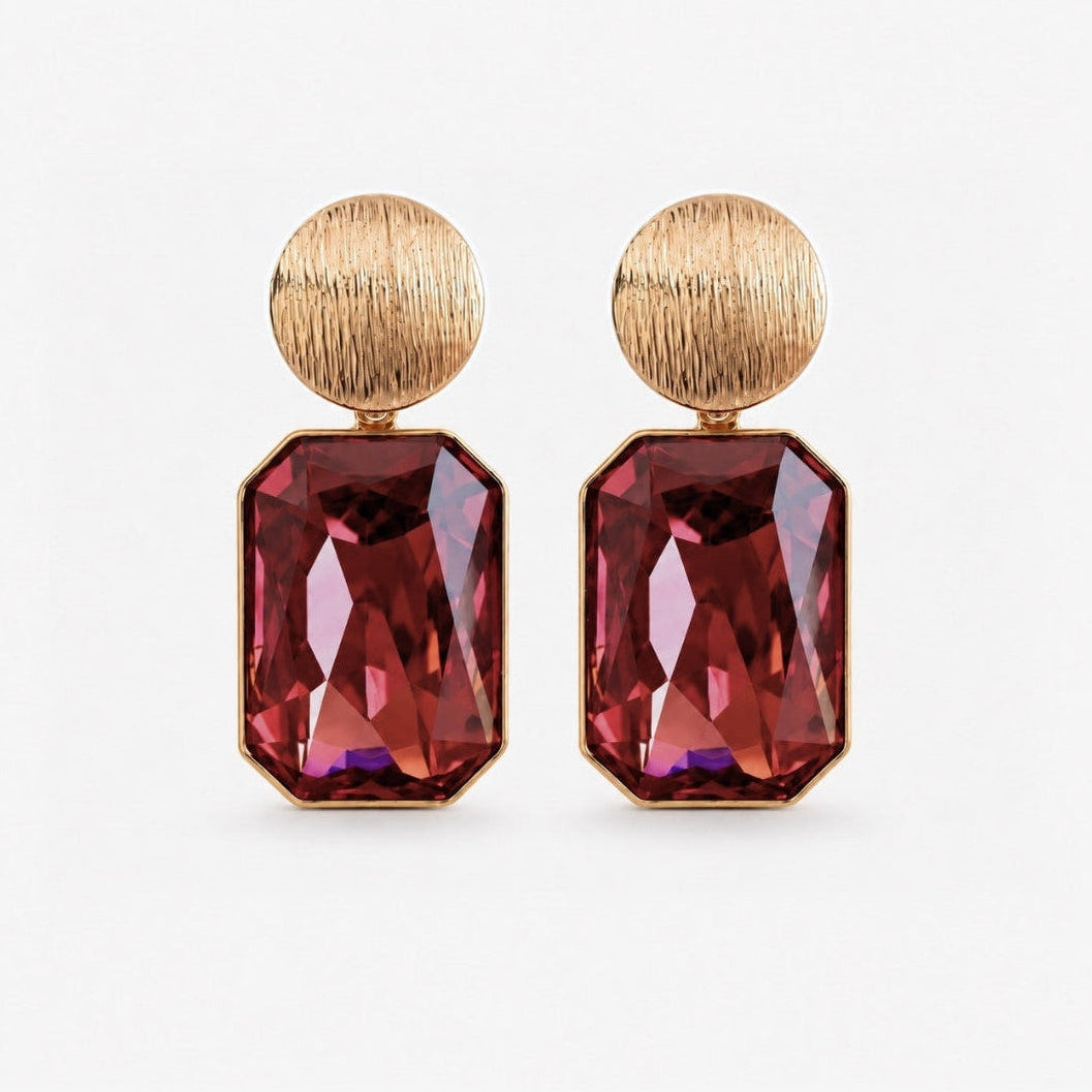 A pair of drop earrings featuring textured gold-tone circular studs and large faceted rectangular ruby-red gemstones, shown on a clean white background.