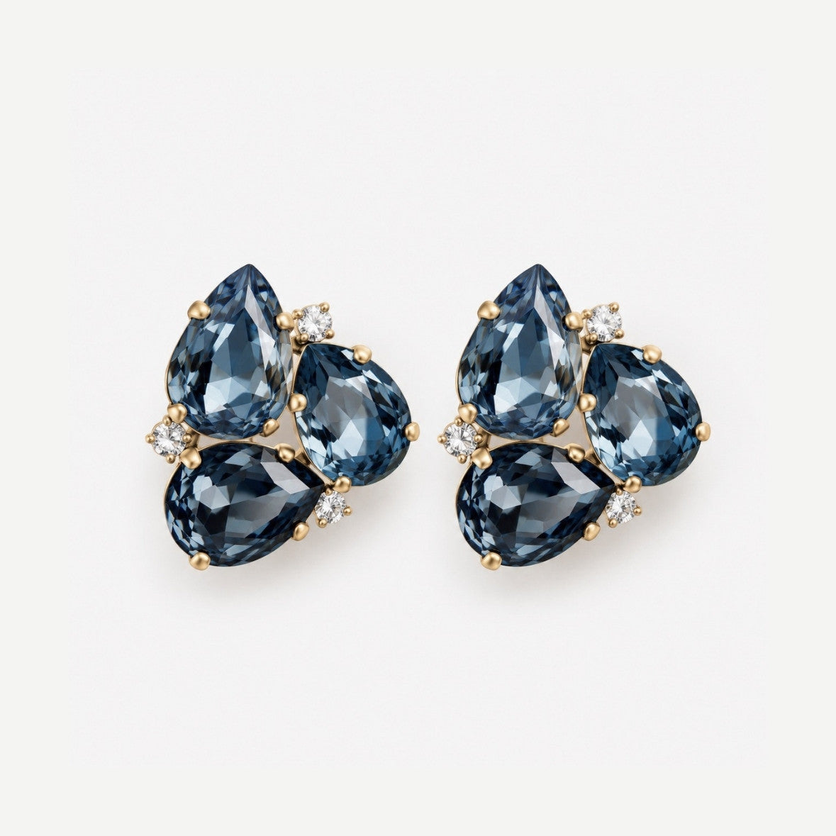 A pair of gold stud earrings featuring three pear-cut dark blue gemstones and small clear accent stones, set against a plain white background.