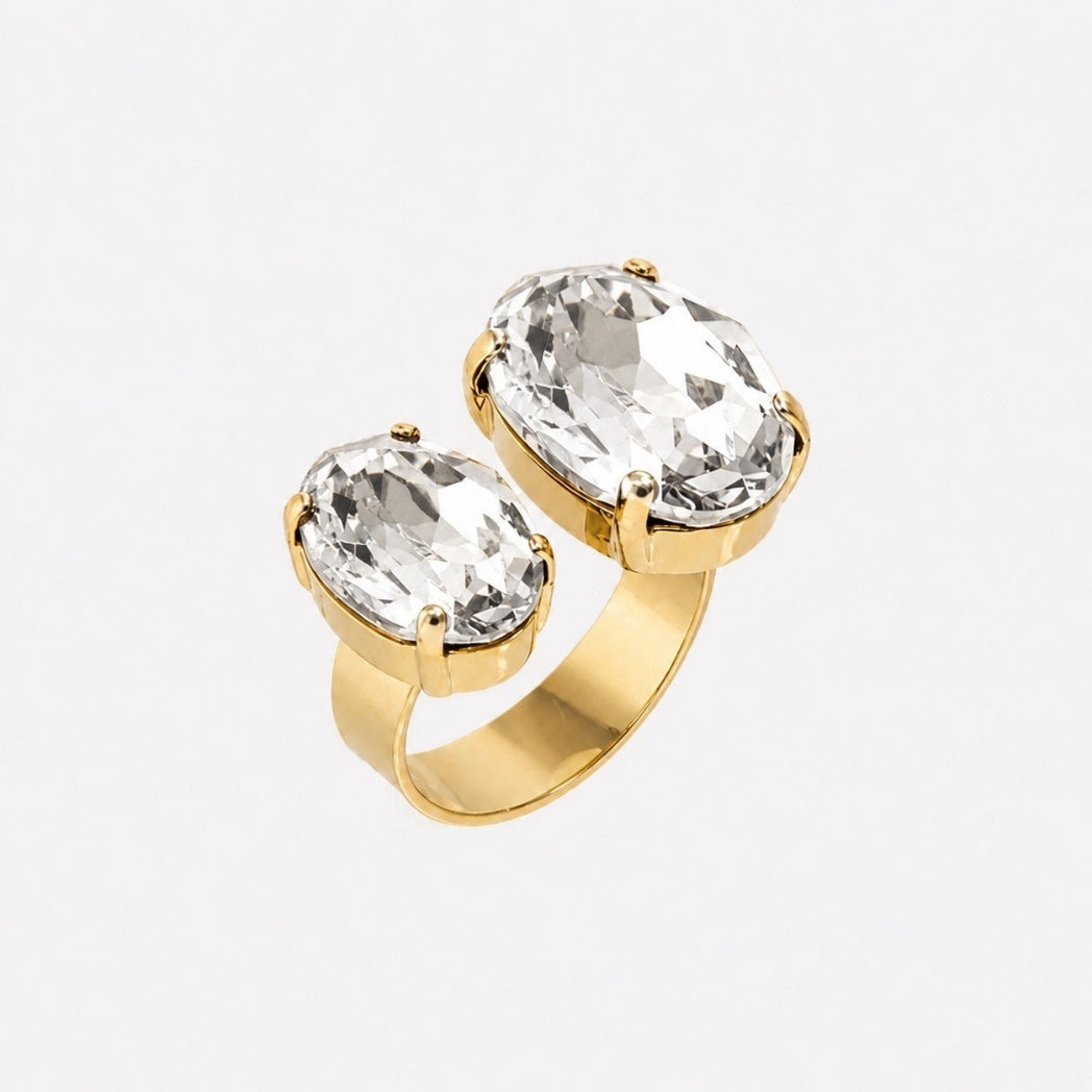 A gold ring featuring two large, oval-cut clear gemstones in a prong setting, shown against a plain light gray background.