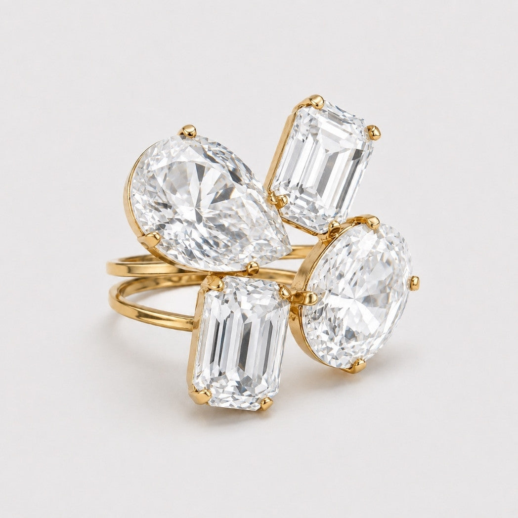 A gold ring featuring four clear gemstones in varied shapes including pear, emerald, and oval, set against a clean white background.