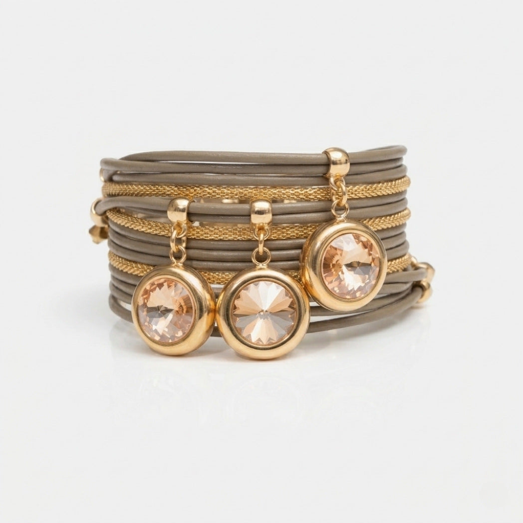 Stack of gray bracelets with gold accents and crystal pendants on a light gray background