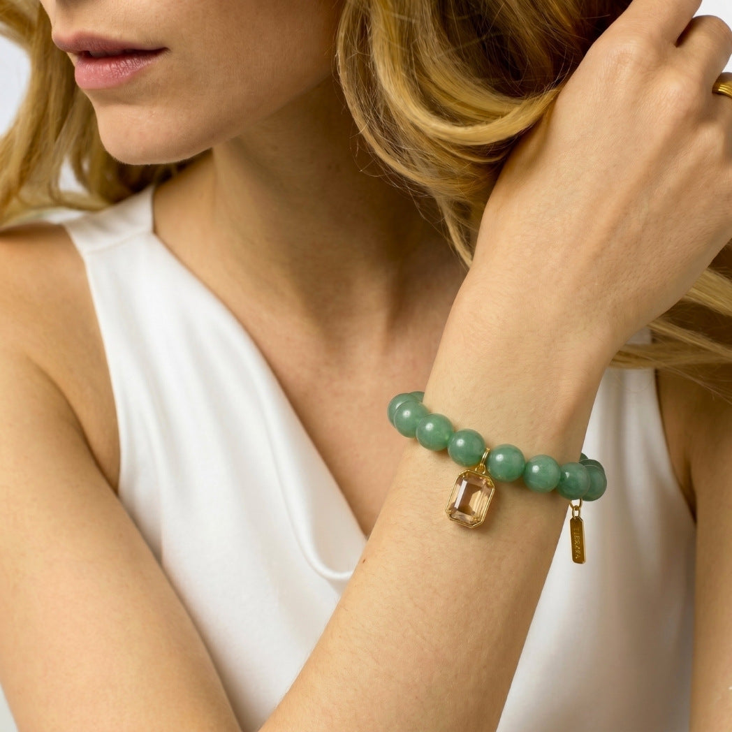 Woman wearing a green beaded bracelet with gold accents on a neutral background