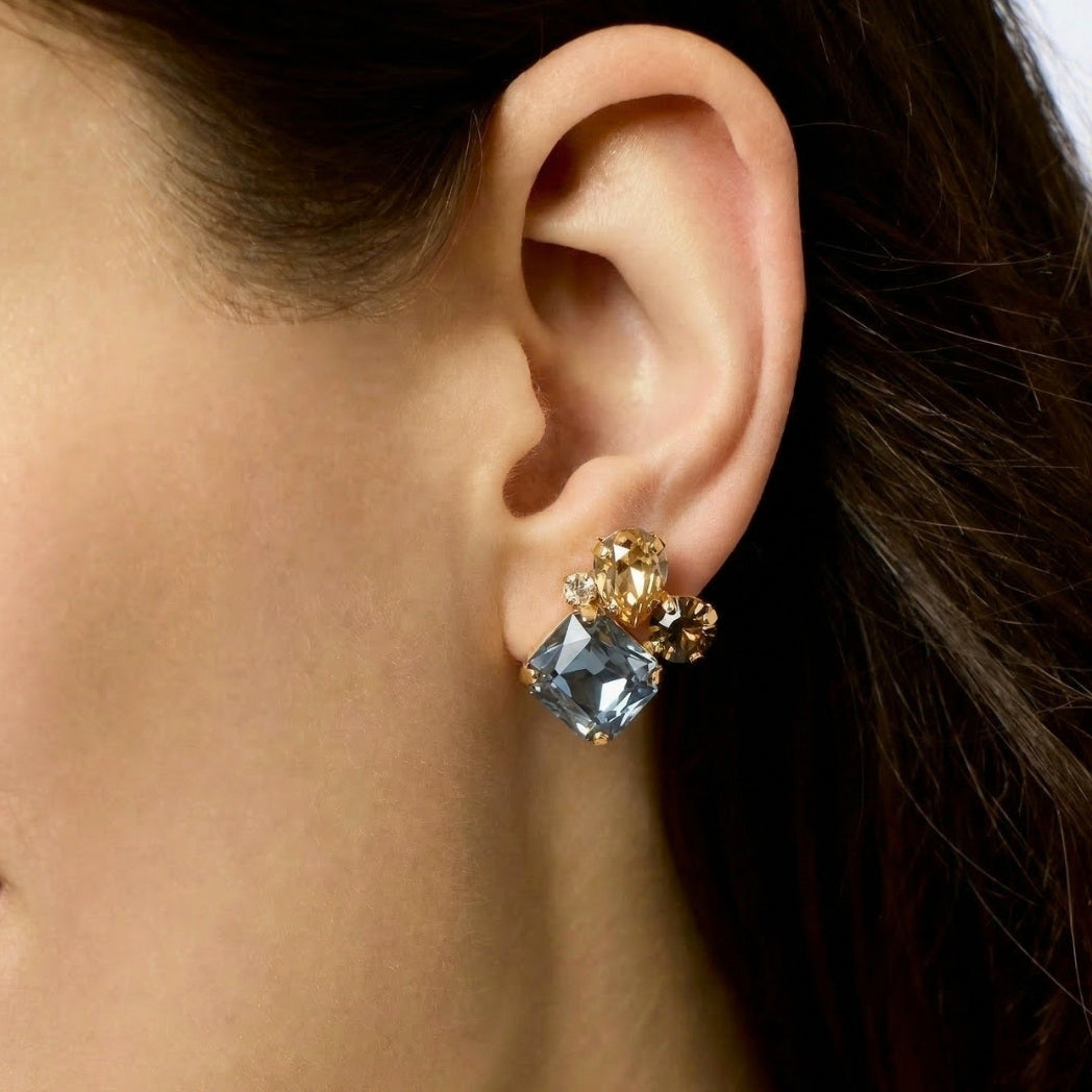Close-up of an ear wearing a sparkling earring with blue and gold stones.