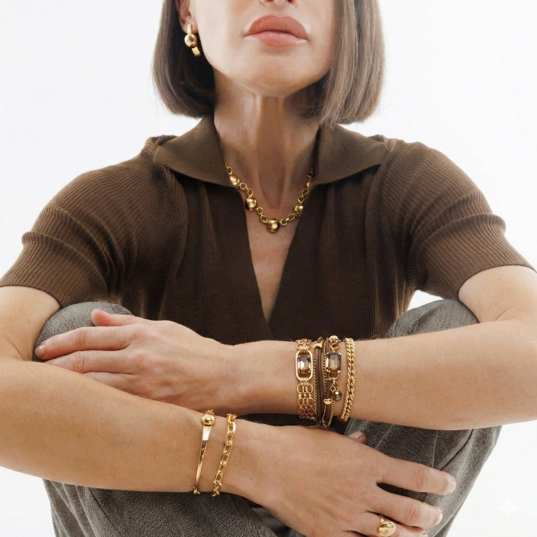 Woman wearing gold jewelry including a necklace, bracelets, and rings on a white background