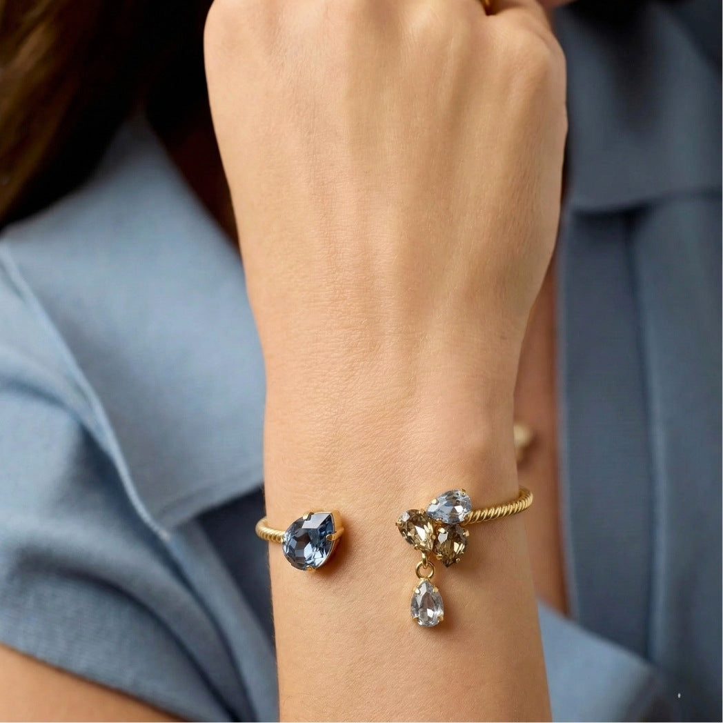 Gold bracelet with gemstones on a person's wrist against a blurred background