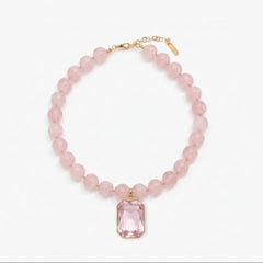 Pink beaded necklace with a rectangular pink gemstone pendant on a white background
