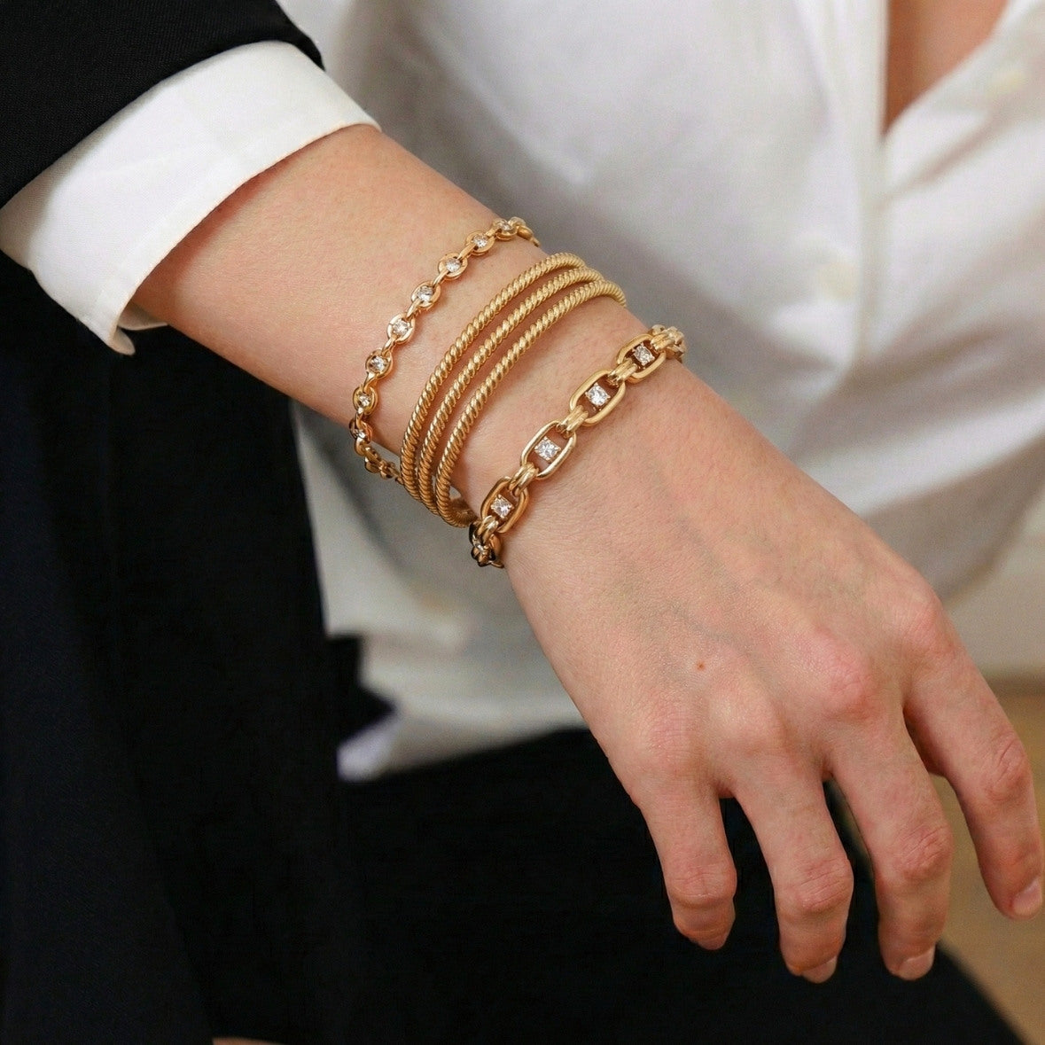 Close-up of a wrist wearing multiple gold bracelets with a blurred background