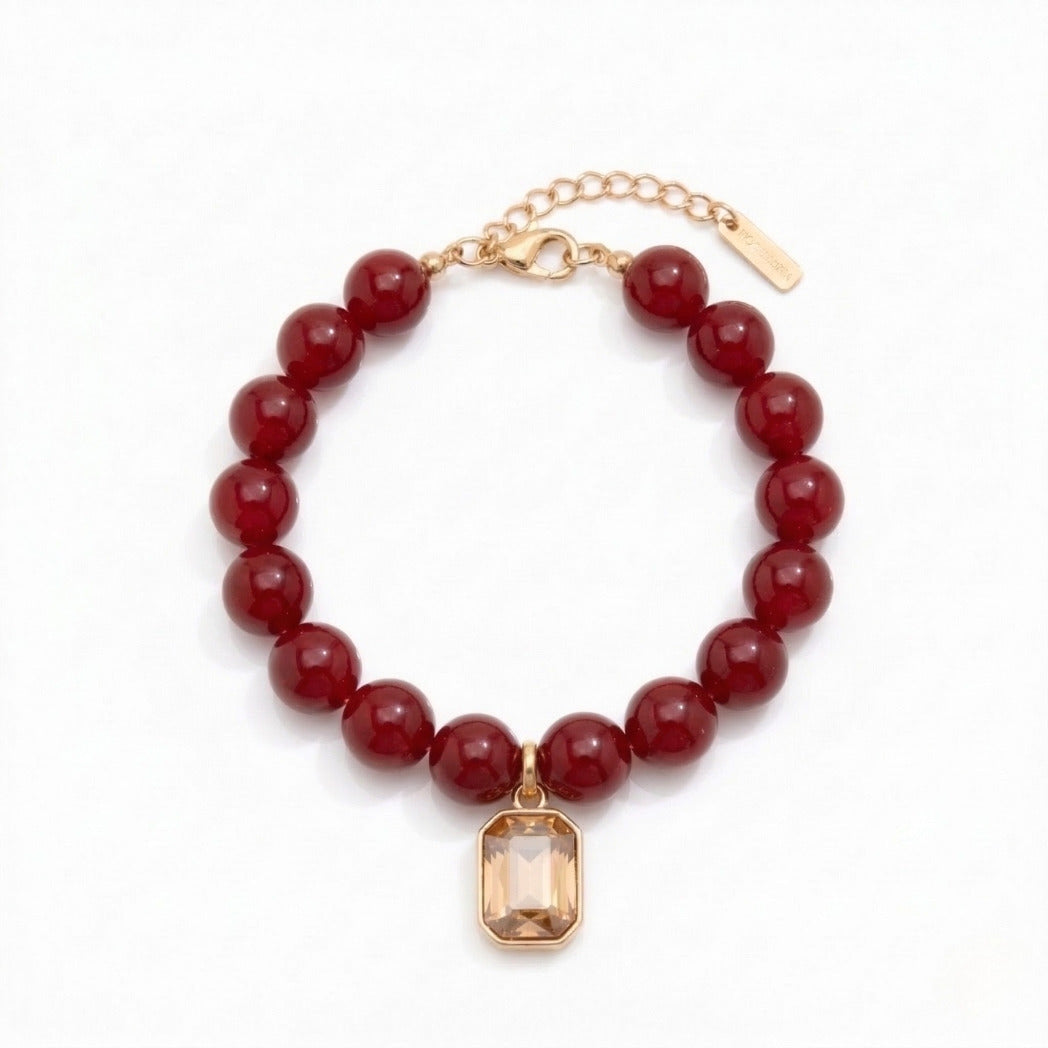 Bracelet with red beads and a gold charm on a white background