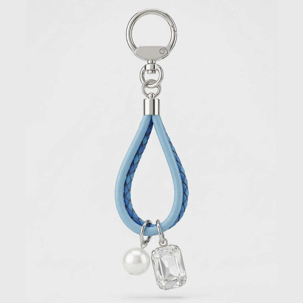 Keychain with blue leather strap, pearl, and clear gemstone charm on a light gray background