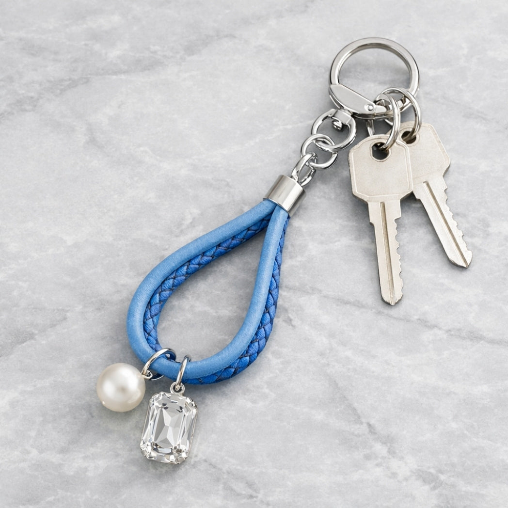 Keychain with blue braided strap, pearl, and clear stone charm on a light gray background
