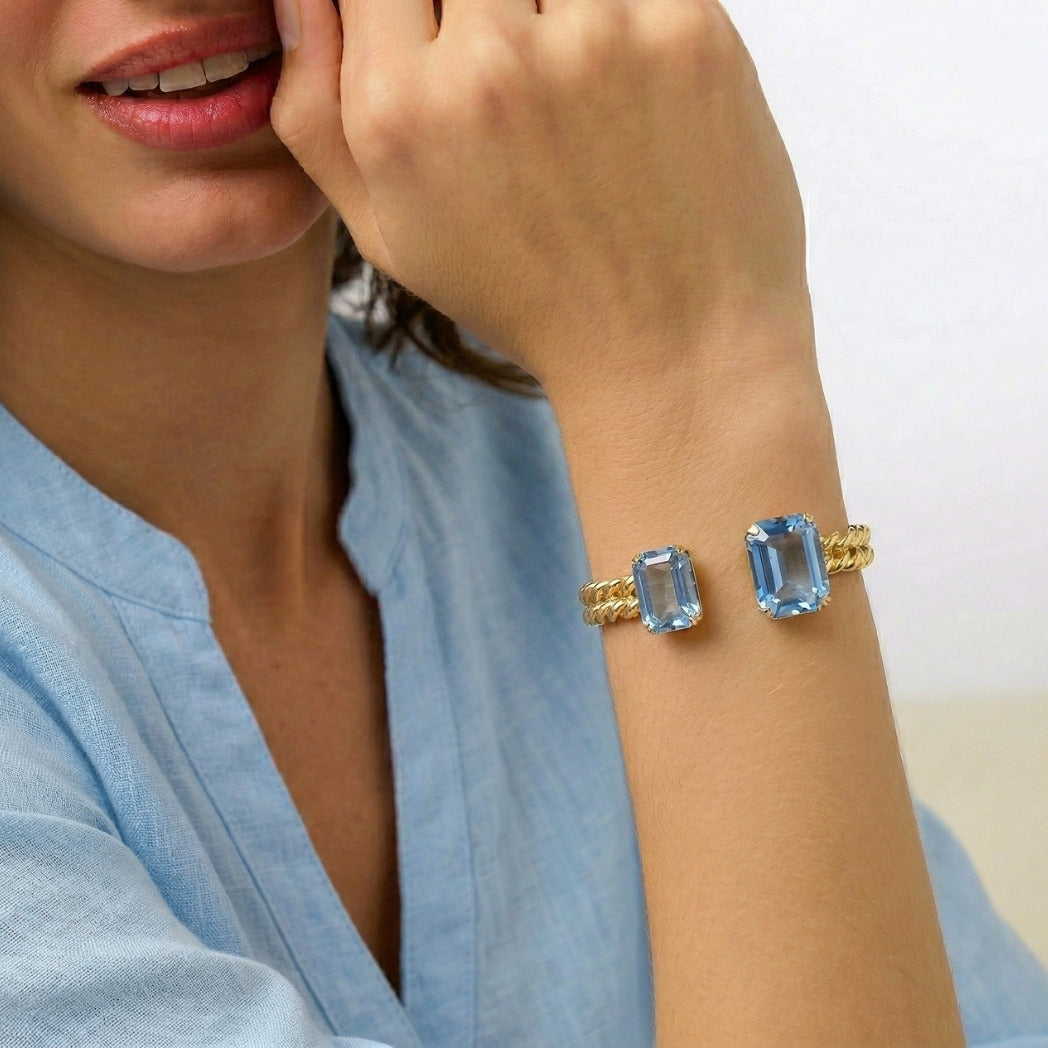 Woman wearing a gold bracelet with blue gemstones on a blurred background
