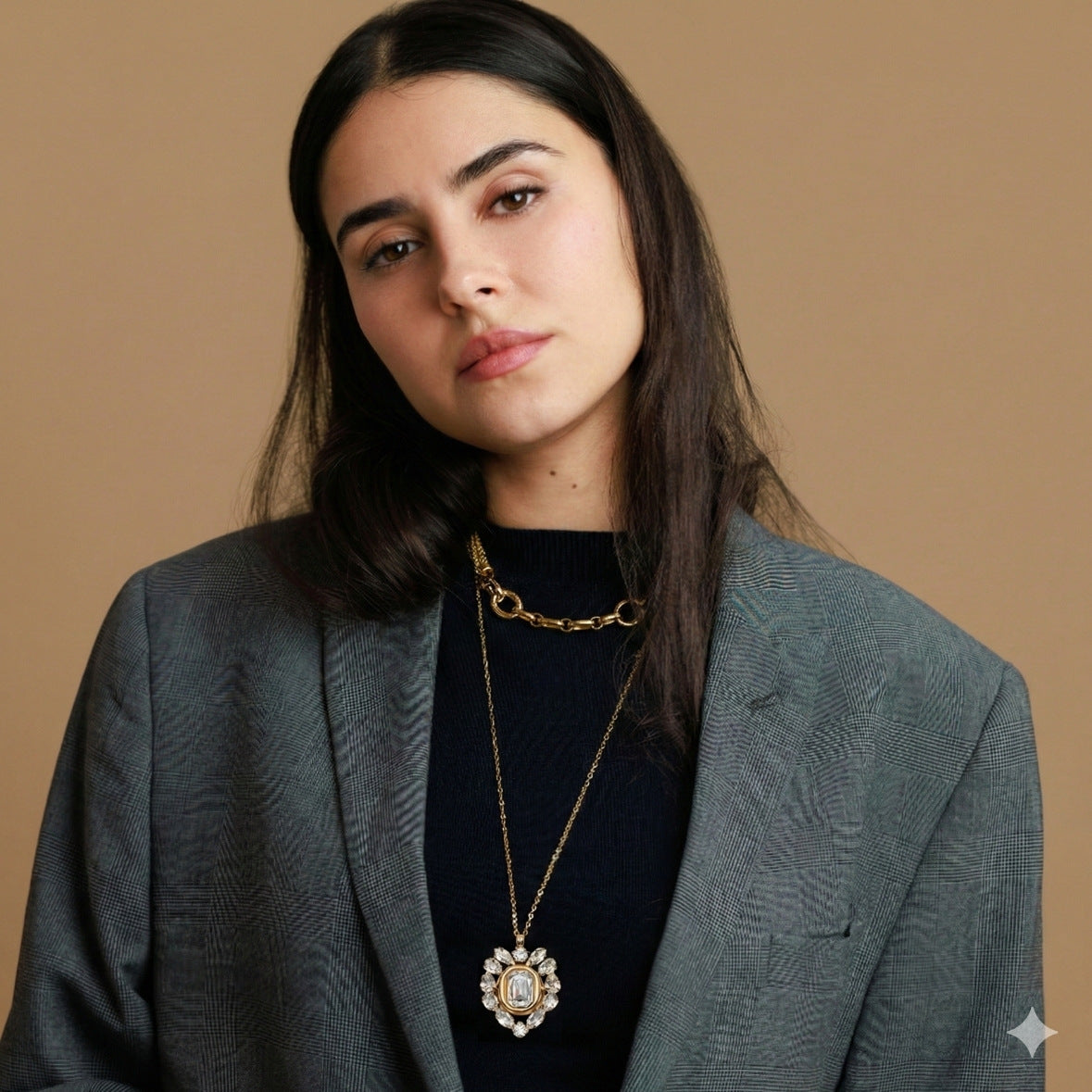 Woman wearing a gray blazer and gold necklace against a beige background