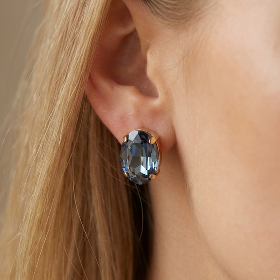 Close-up of an ear wearing a blue gemstone earring with a neutral background