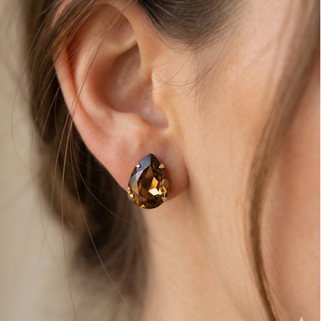 Close-up of an ear wearing a smoky brown gemstone earring against a neutral background