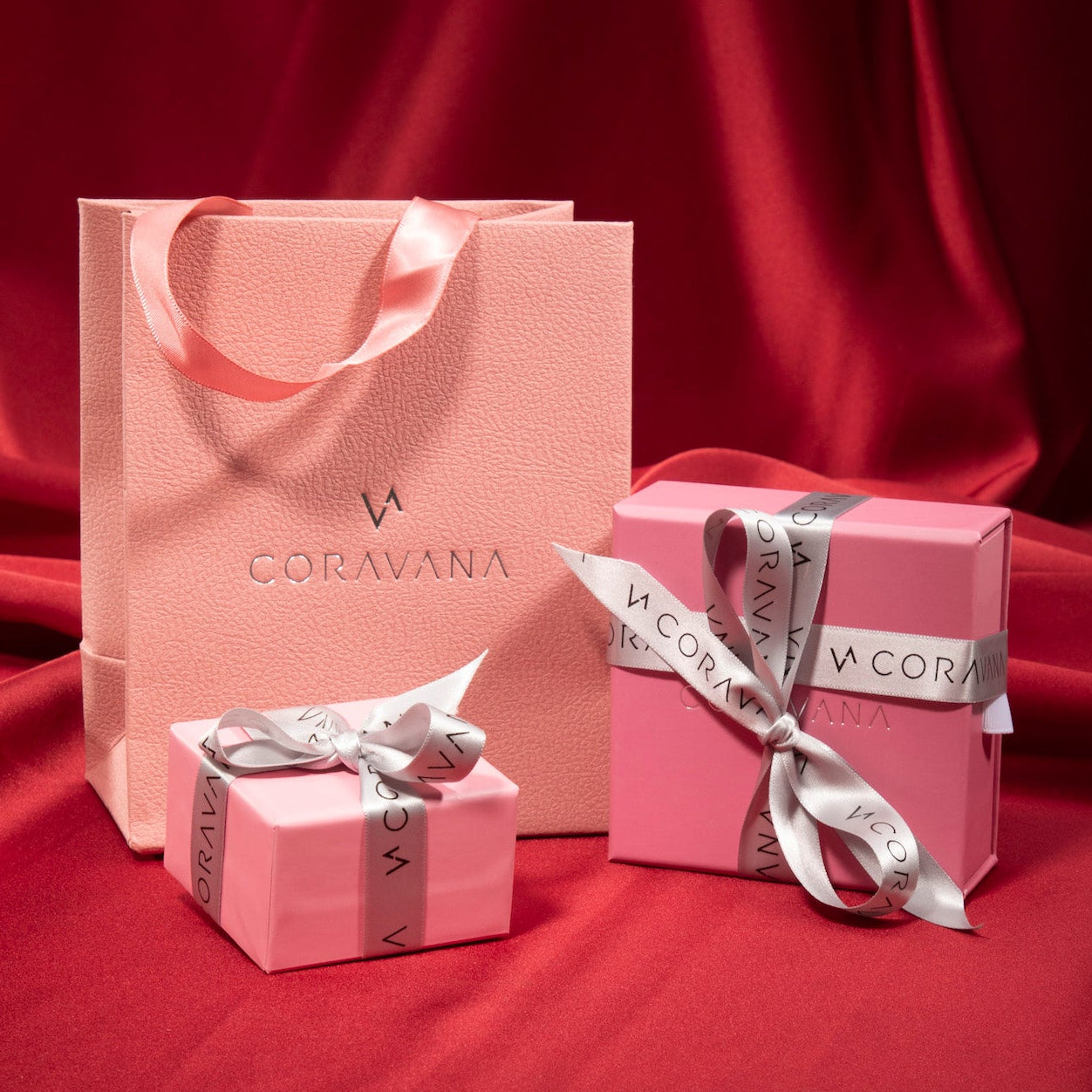 Pink 'CORAVANA' gift bag and boxes with ribbons on a red fabric background