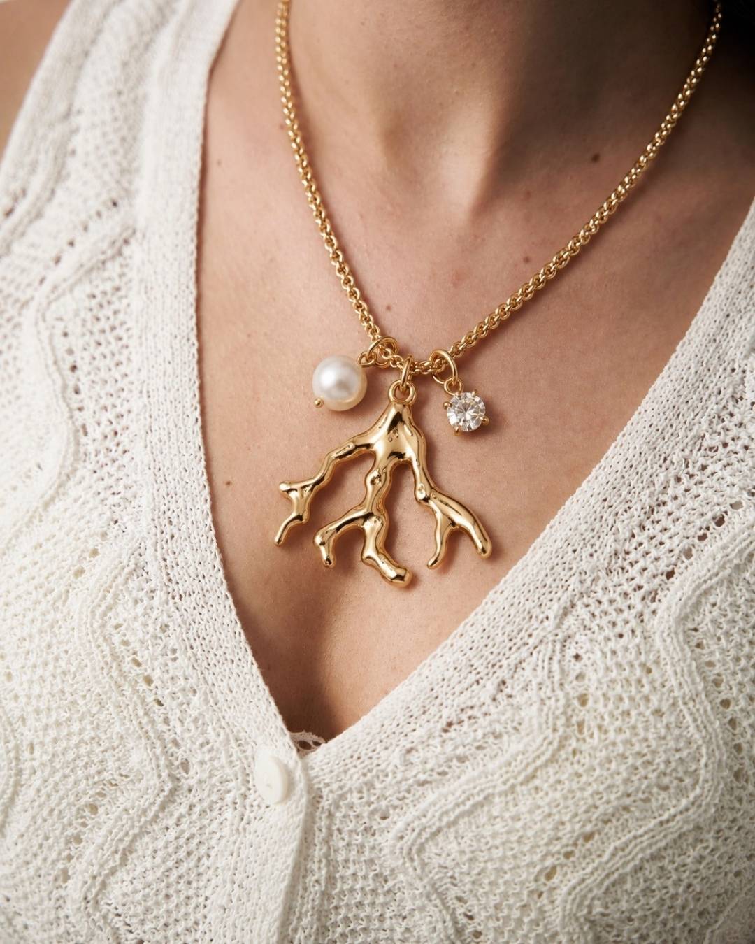 Gold necklace with coral and pearl pendant on a person wearing a white sweater.