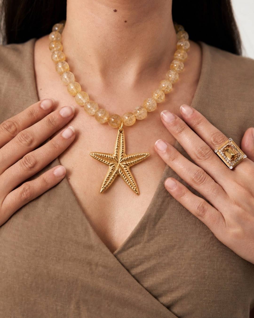 Person wearing a gold starfish necklace and ring with a neutral background
