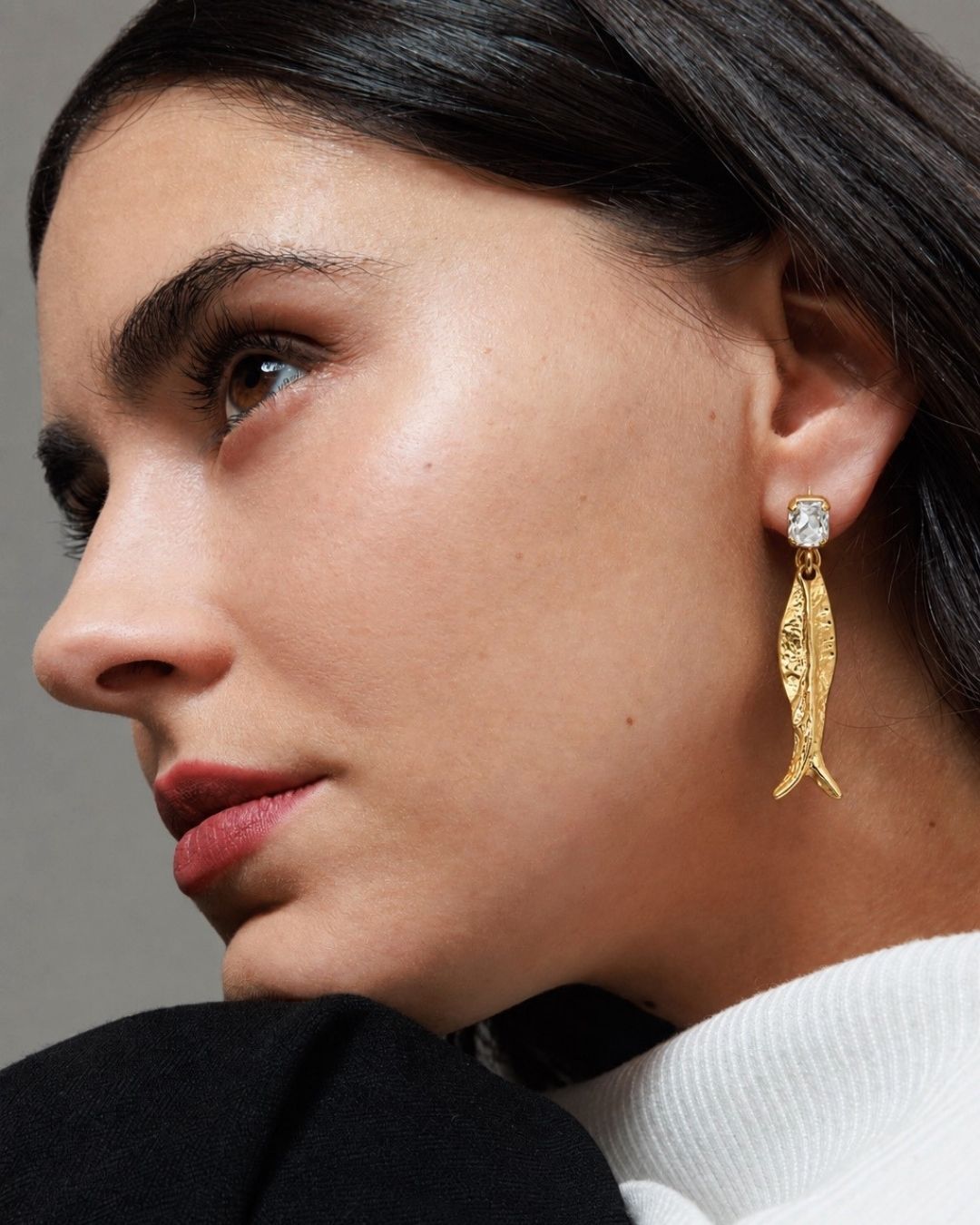 Close-up of a woman wearing gold earrings with a neutral background