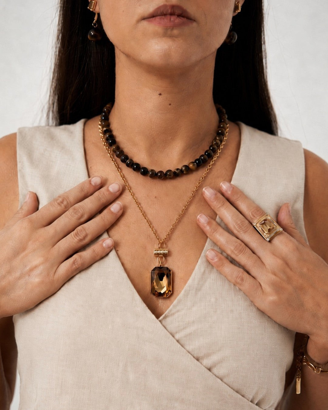 Woman wearing gold necklace and ring with a neutral background