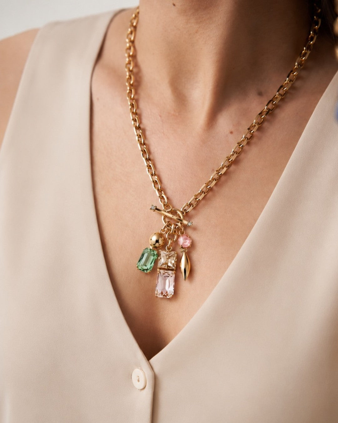 Gold necklace with colorful charms worn by a person in a beige top.
