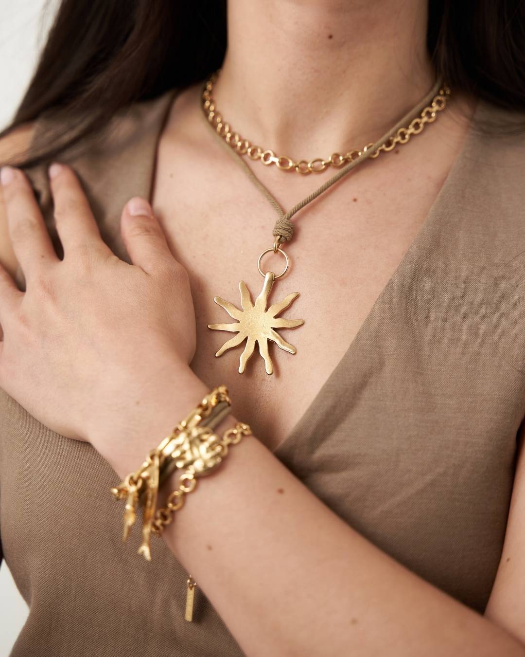 Person wearing a gold necklace and bracelet with a sun pendant.