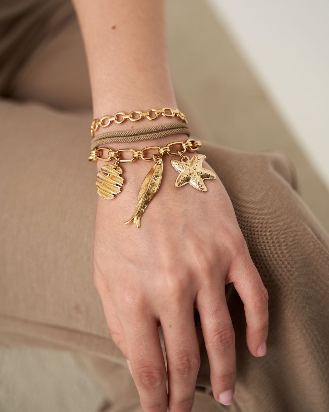 Gold bracelet with charms on a hand against a neutral background