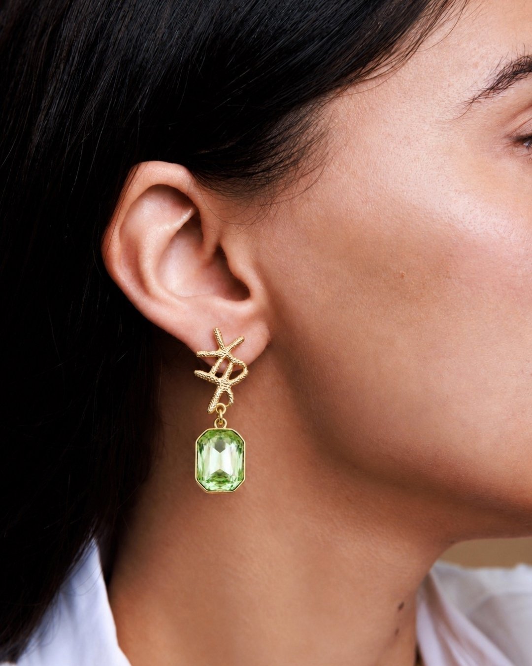 Close-up of a person wearing a gold earring with a green gemstone.