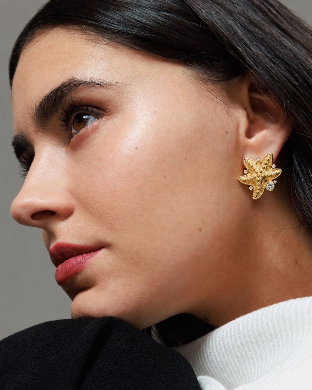 Close-up of a woman wearing a gold earring with a gray background