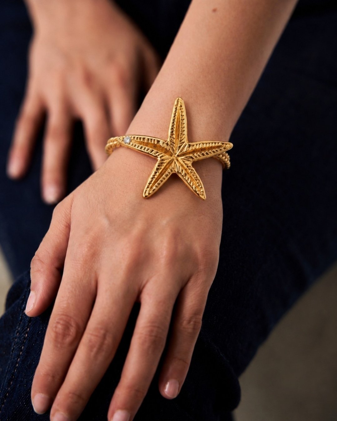 Gold starfish bracelet on a person's wrist with a dark background