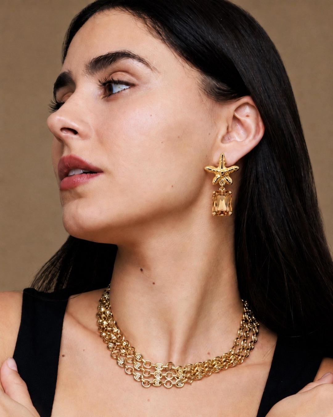 Woman wearing gold earrings and necklace against a brown background