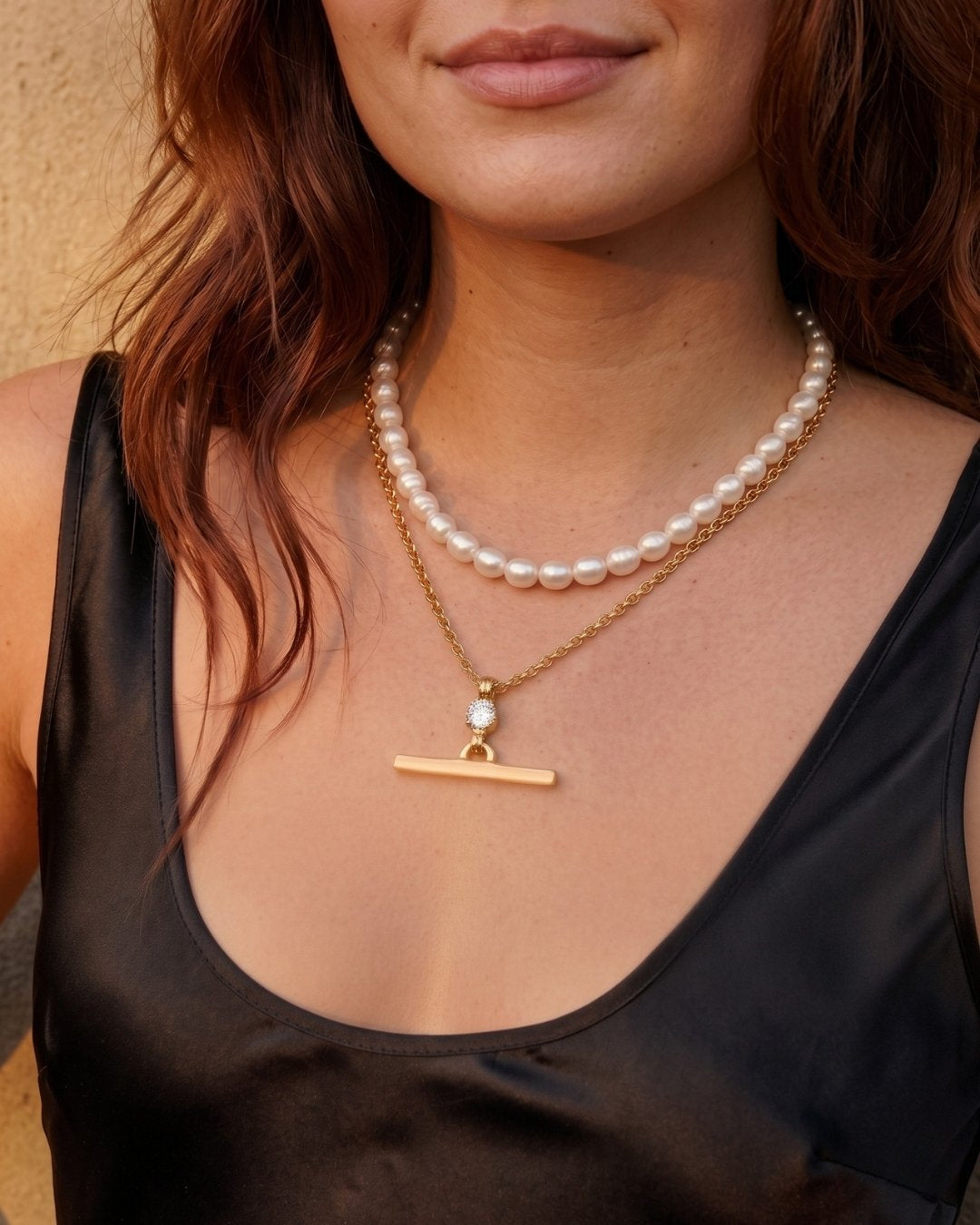Woman wearing a pearl necklace with a gold clasp on a plain background