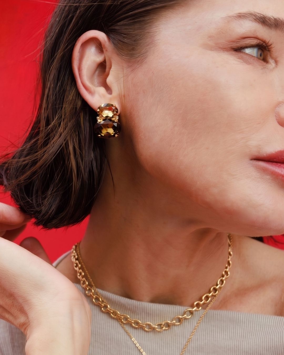 Close-up of a woman wearing gold hoop earrings and necklaces against a red background
