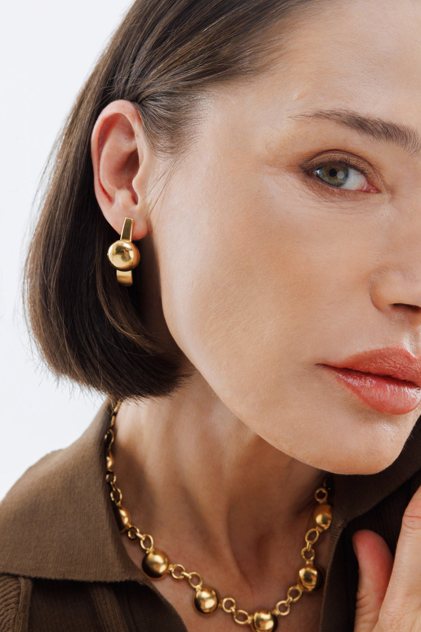 Close-up of a woman wearing gold earrings and necklace against a neutral background