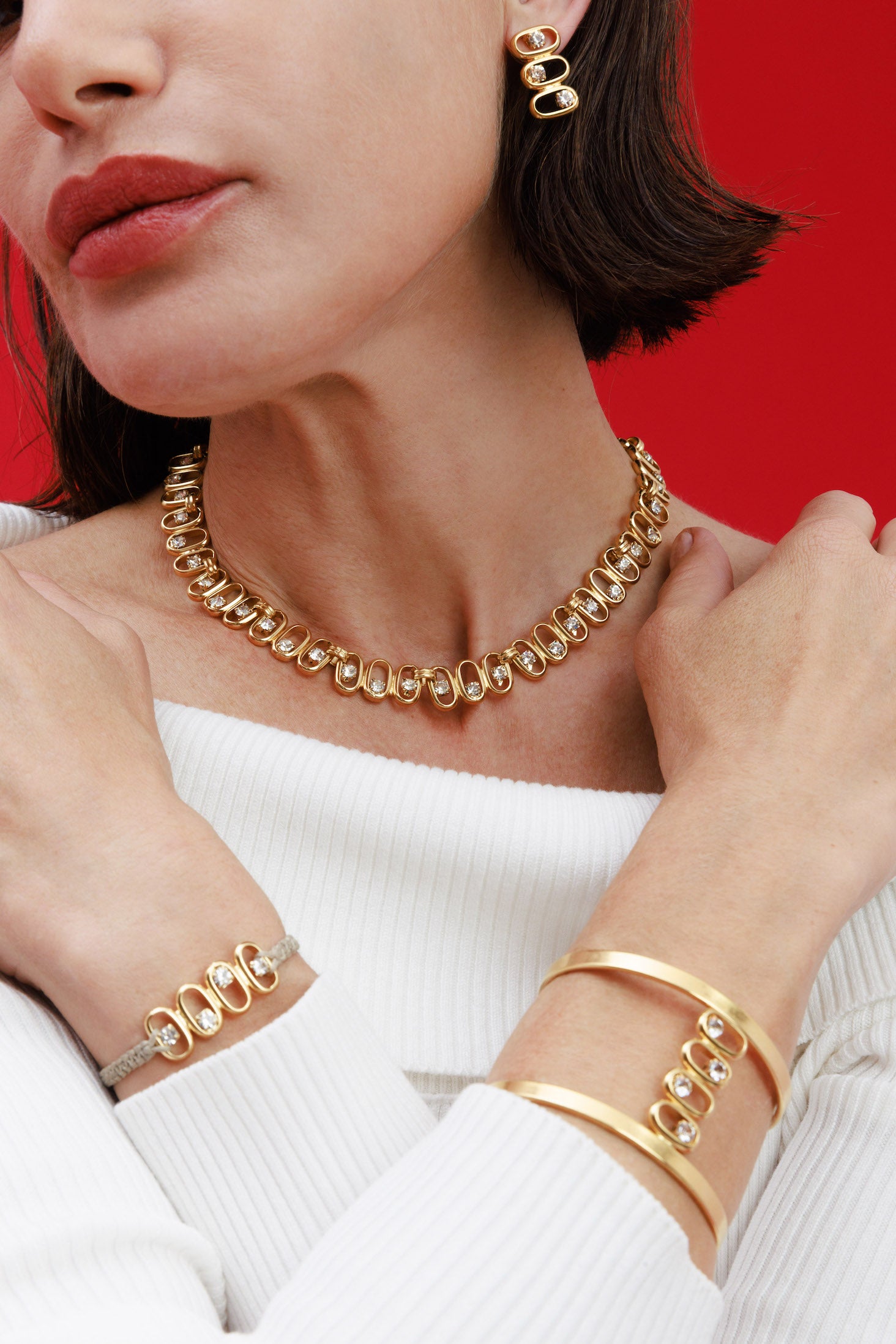 Woman wearing gold jewelry including a necklace, bracelet, and hoop earrings against a red background