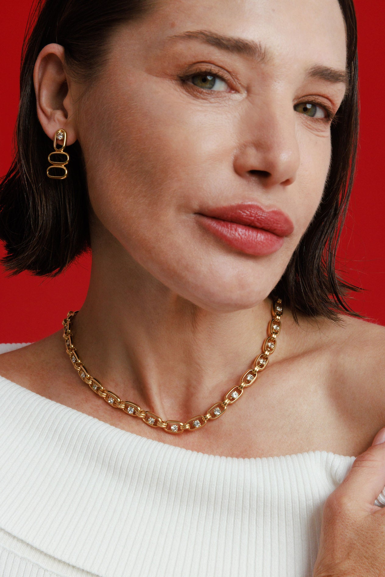 Woman wearing a gold necklace and earrings against a red background