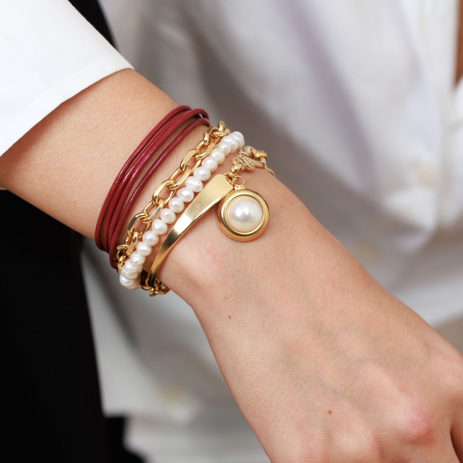 Close-up of a wrist wearing multiple bracelets with a focus on gold and pearl design.