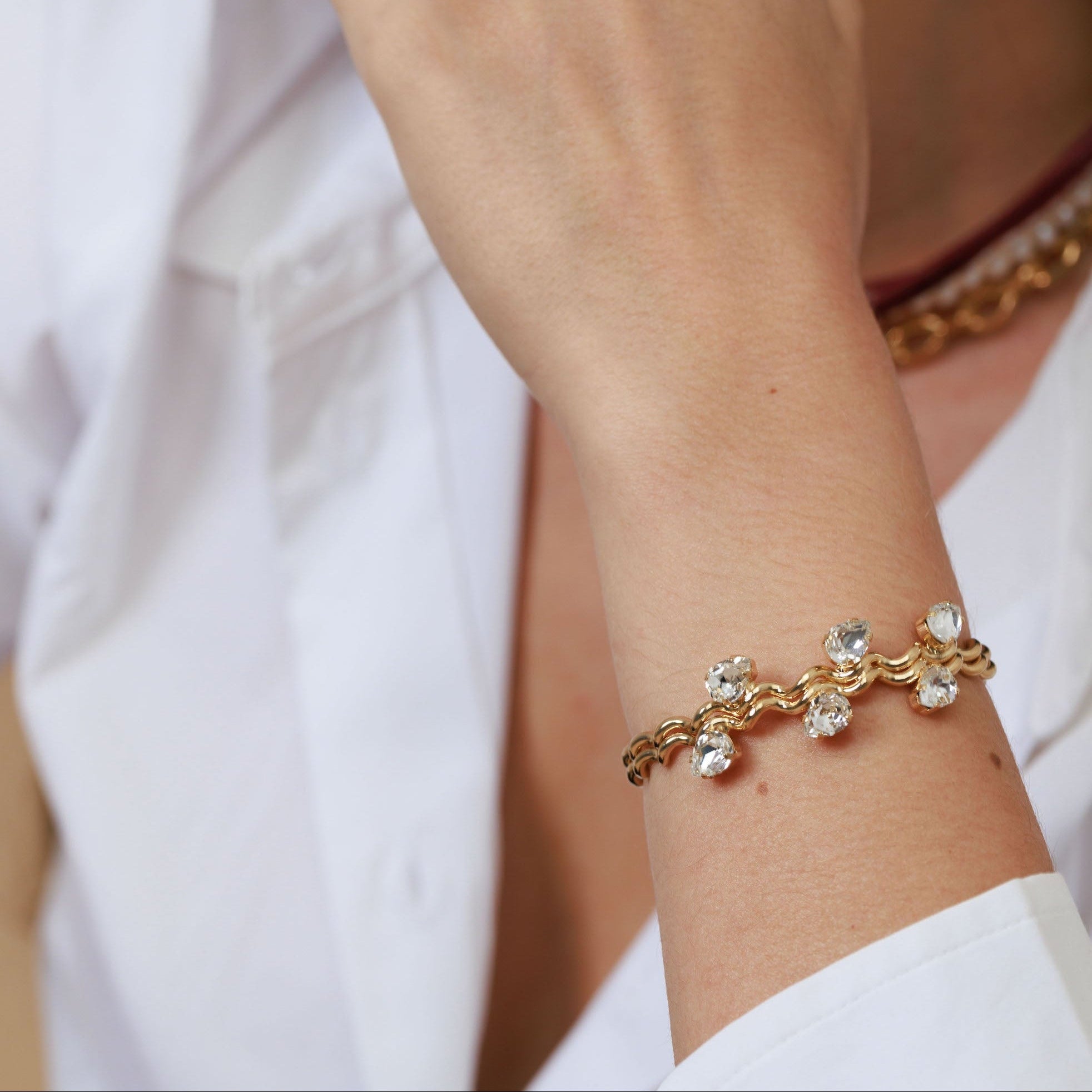 Close-up of a person wearing a gold bracelet with clear stones on a neutral background