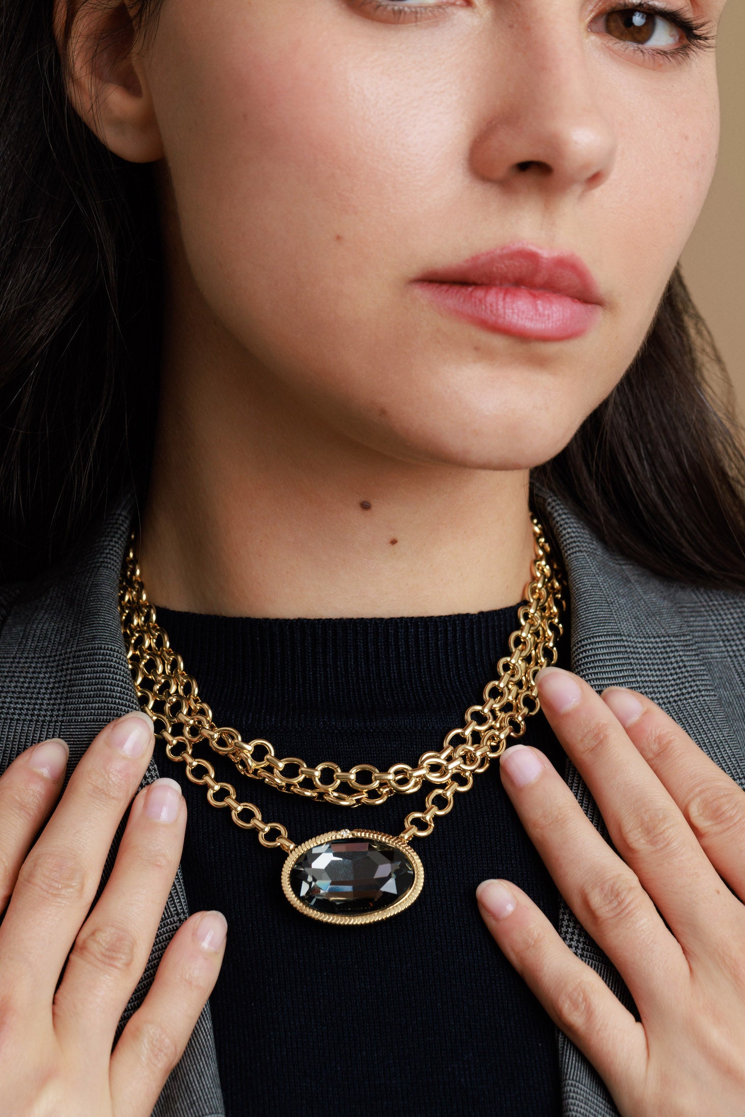 Woman wearing a gold chain necklace with a dark stone pendant.