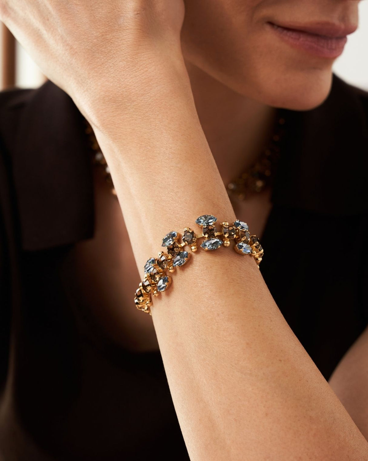 A close-up of a model's wrist wearing a gold-toned bracelet adorned with light blue faceted gemstones.
