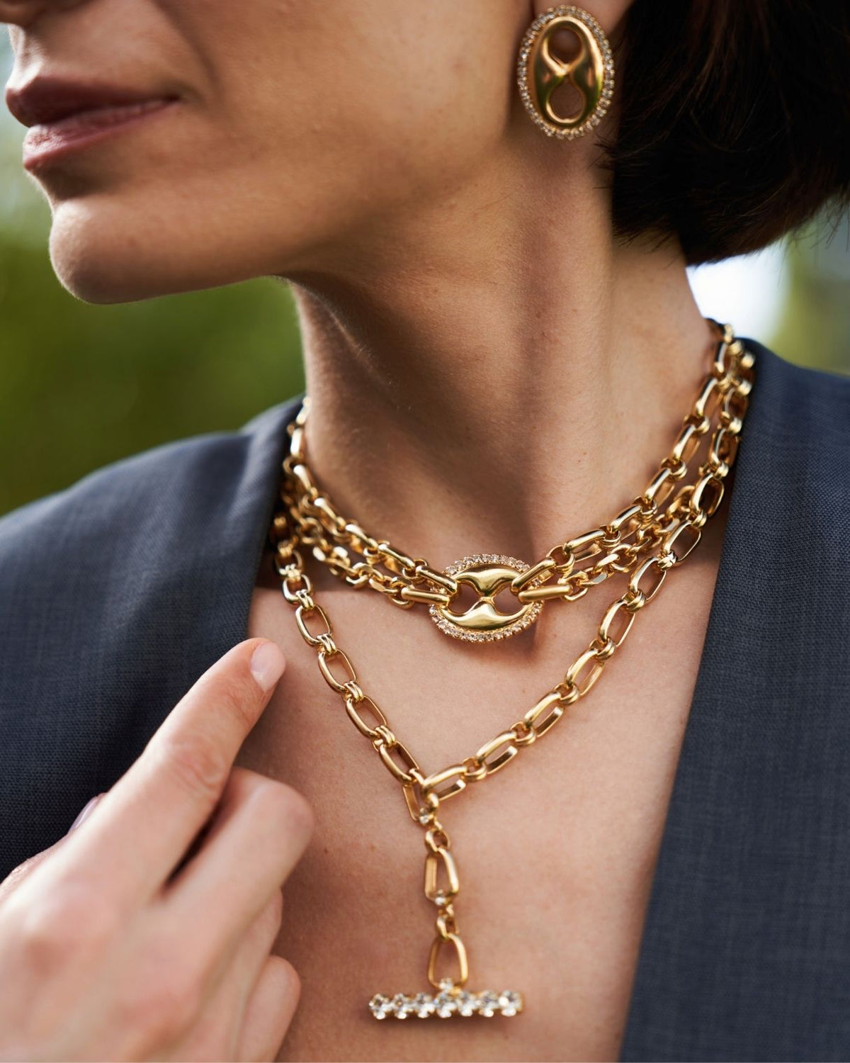 A close-up lifestyle shot of a model wearing a multi-layered gold chain necklace with a Y-shaped pendant and a matching gold earring.