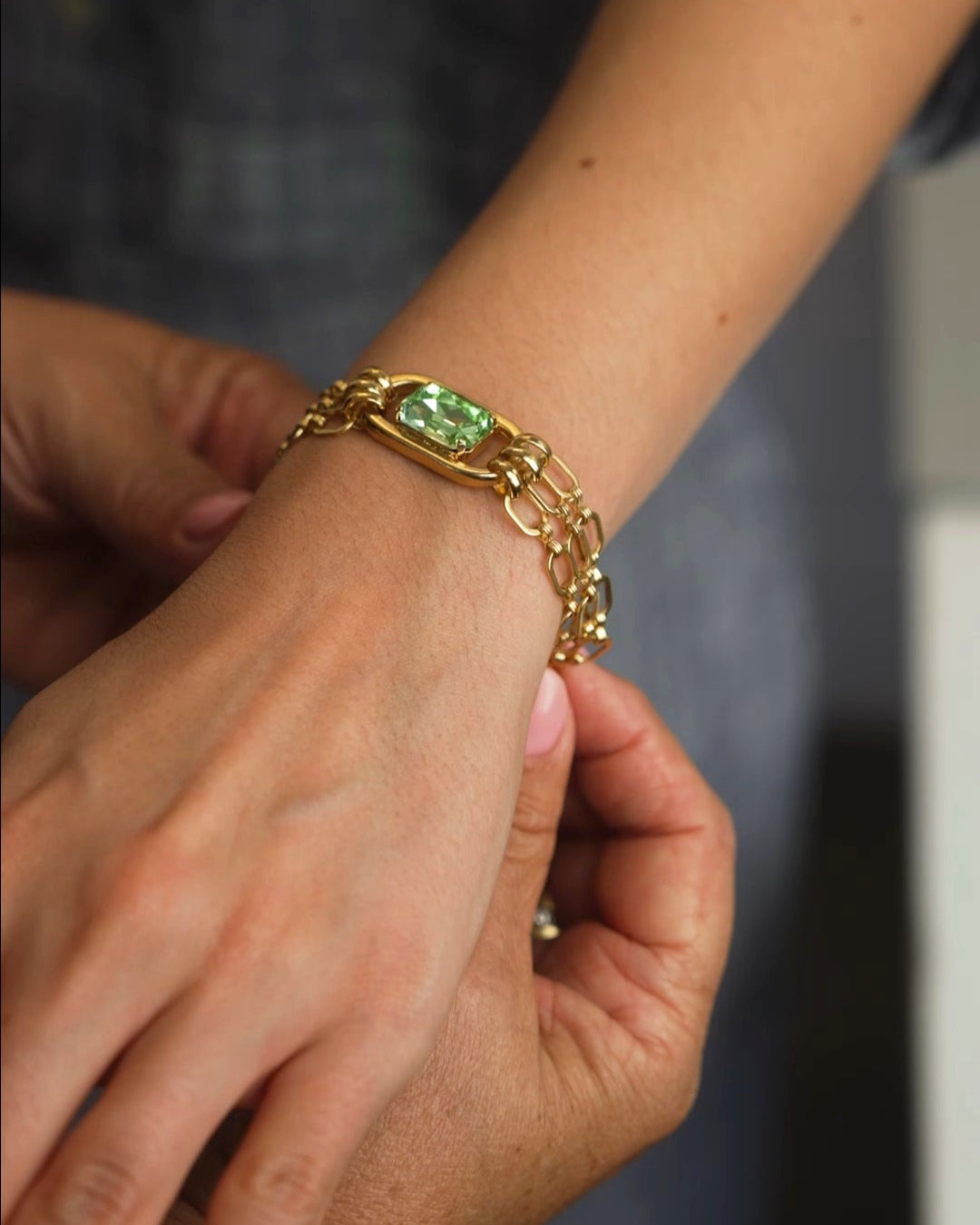 Gold bracelet with a green gemstone on a wrist against a dark background