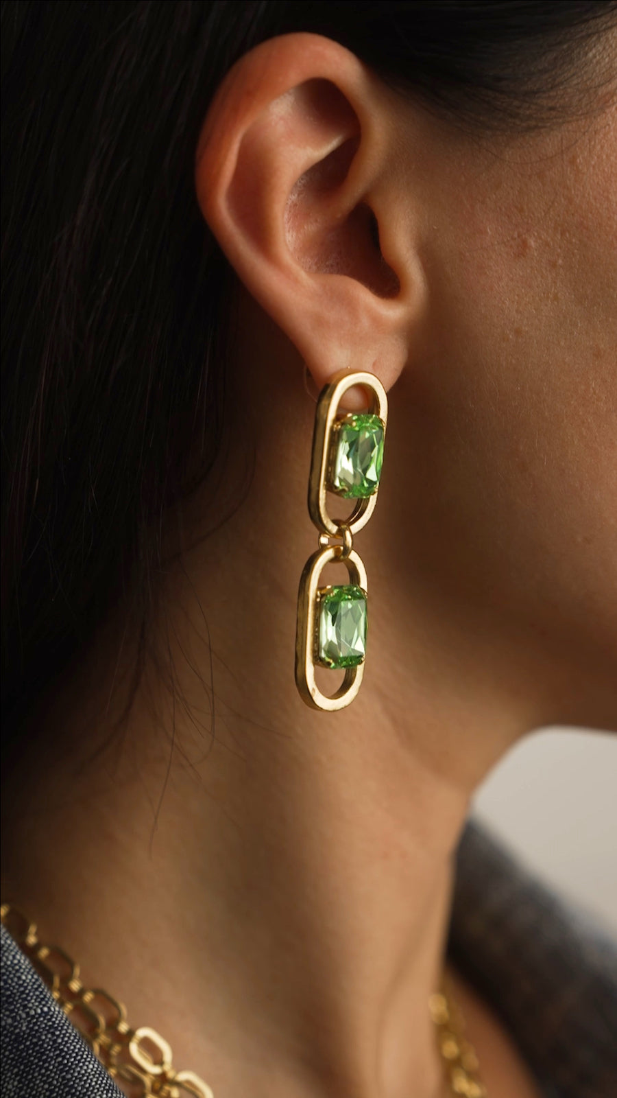 Gold earring with green gemstones worn by a person