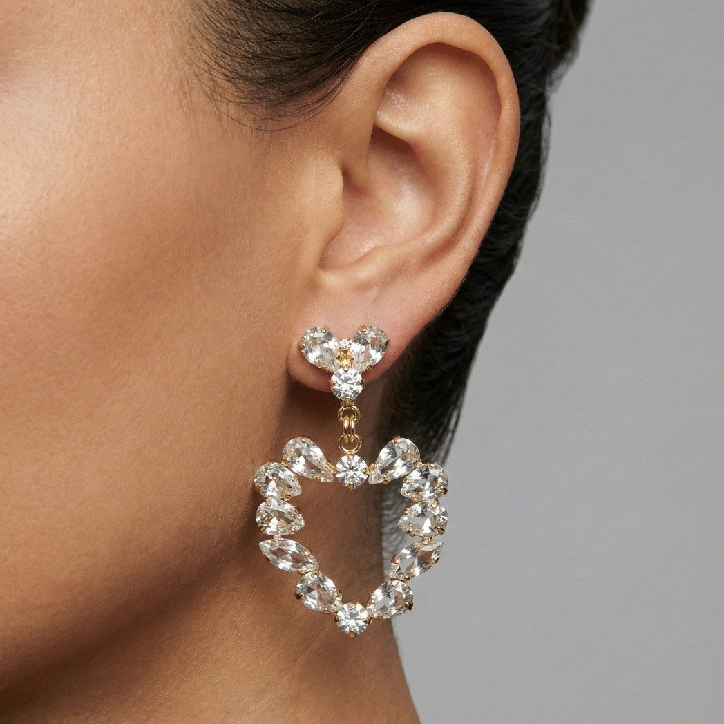 Close-up of a woman's ear wearing a pair of diamond hoop earrings with a gray background.